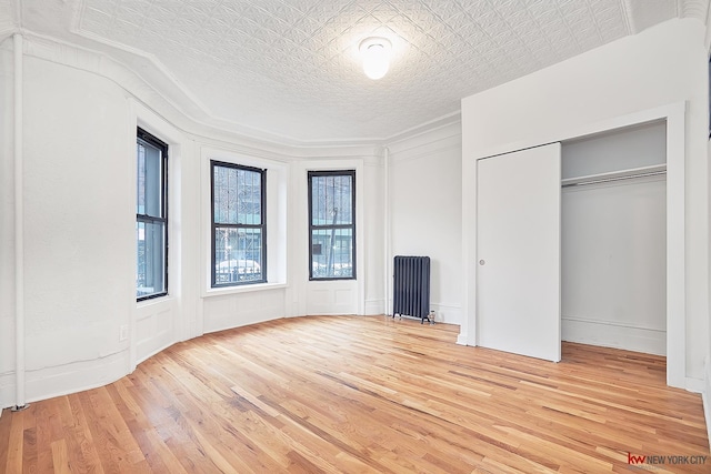 unfurnished bedroom with radiator heating unit, wood finished floors, a textured ceiling, a decorative wall, and a closet