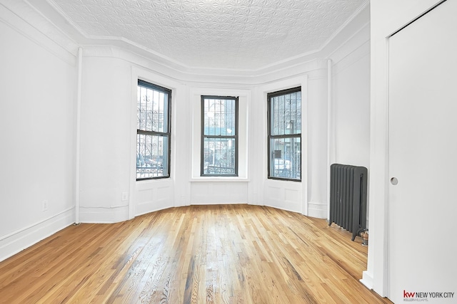 unfurnished room with an ornate ceiling, radiator, ornamental molding, and light wood finished floors