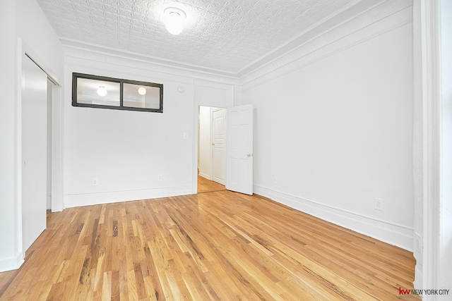 unfurnished room featuring light wood-type flooring, crown molding, a textured ceiling, and baseboards