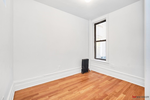 unfurnished room with radiator, light wood-style floors, and baseboards