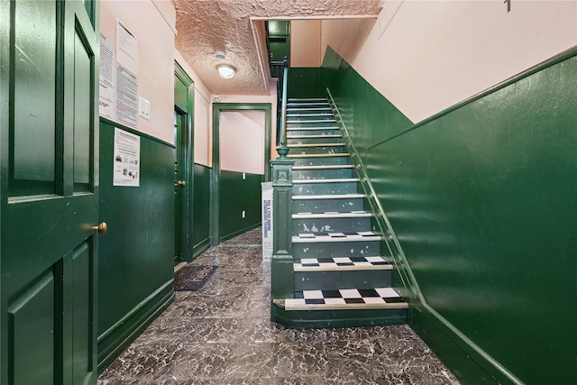 stairway with a textured ceiling and marble finish floor