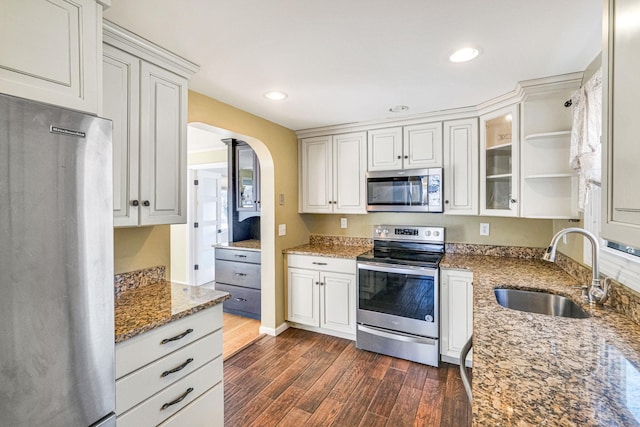 kitchen featuring glass insert cabinets, appliances with stainless steel finishes, dark wood-style flooring, light stone countertops, and a sink