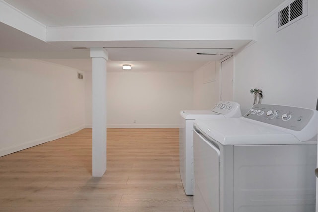 clothes washing area featuring washing machine and dryer, visible vents, light wood-style flooring, and baseboards