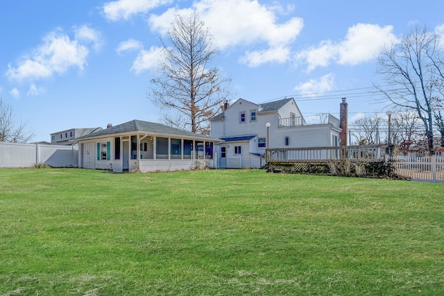 rear view of property featuring a sunroom, a lawn, a wooden deck, and fence