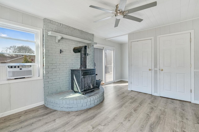 unfurnished living room with a wood stove, baseboards, a ceiling fan, and wood finished floors