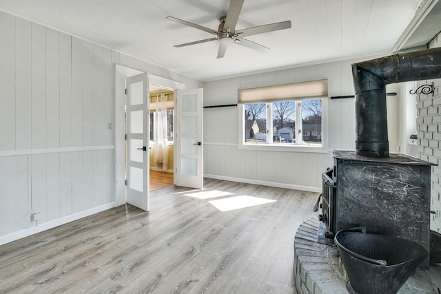 living area featuring a wood stove, baseboards, a ceiling fan, and wood finished floors