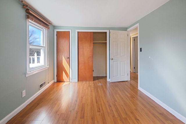 unfurnished bedroom with visible vents, light wood-style flooring, baseboards, and two closets