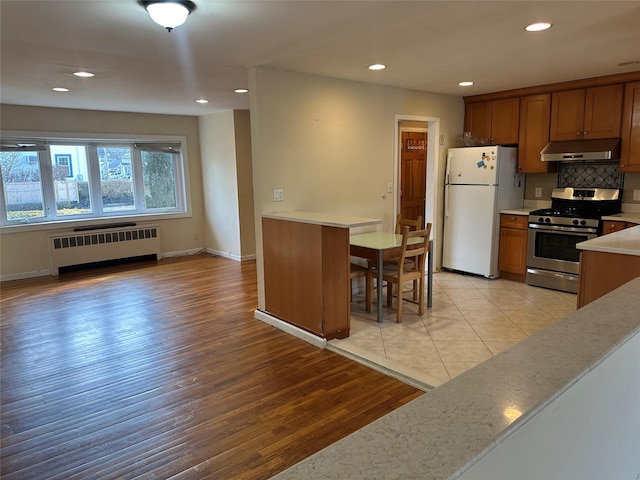 kitchen with radiator, gas range, freestanding refrigerator, light countertops, and under cabinet range hood