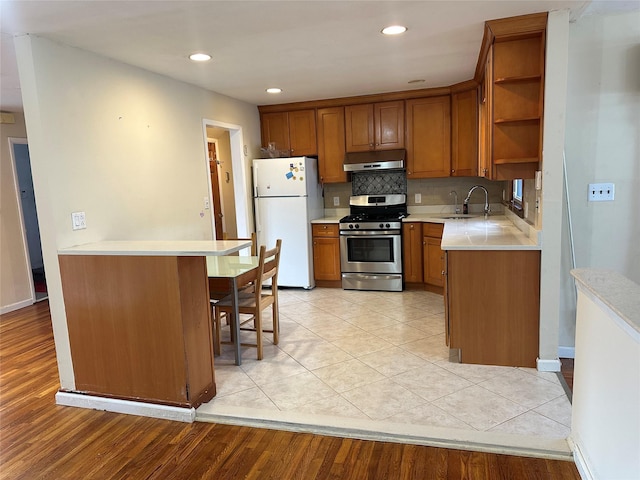 kitchen featuring gas range, brown cabinets, freestanding refrigerator, under cabinet range hood, and open shelves