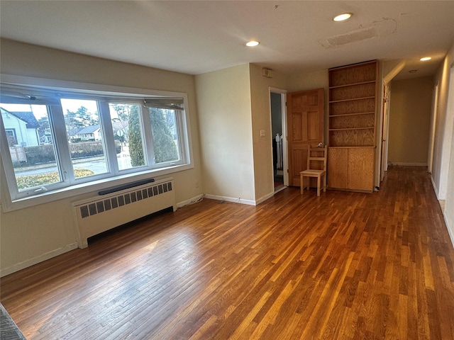 empty room featuring recessed lighting, baseboards, radiator heating unit, and wood finished floors