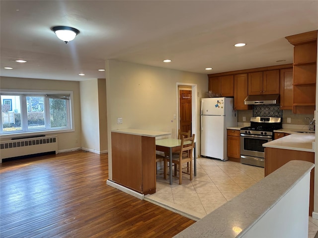 kitchen featuring radiator, freestanding refrigerator, under cabinet range hood, open shelves, and stainless steel range with gas stovetop