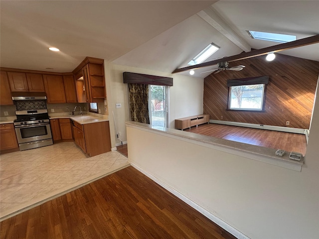 kitchen with open shelves, light countertops, brown cabinetry, stainless steel gas stove, and under cabinet range hood