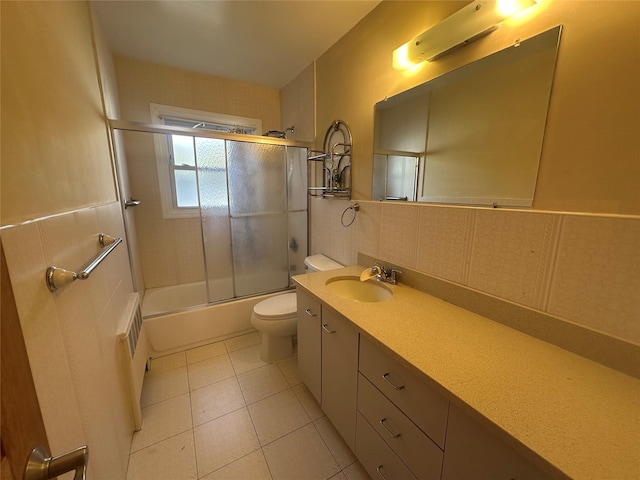 full bathroom with tile walls, bath / shower combo with glass door, toilet, vanity, and tile patterned flooring