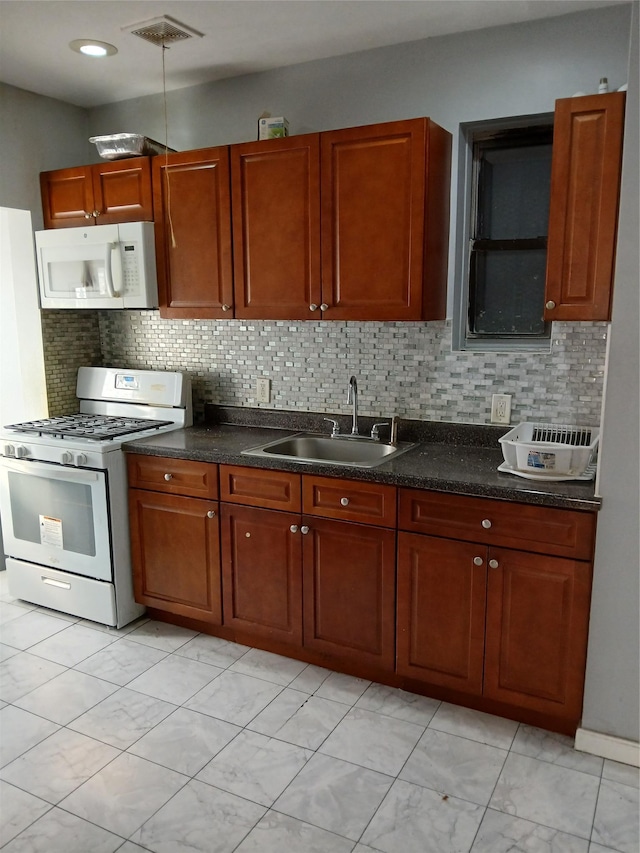 kitchen with white appliances, dark countertops, a sink, and visible vents