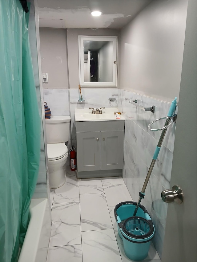 bathroom with marble finish floor, tile walls, toilet, wainscoting, and vanity