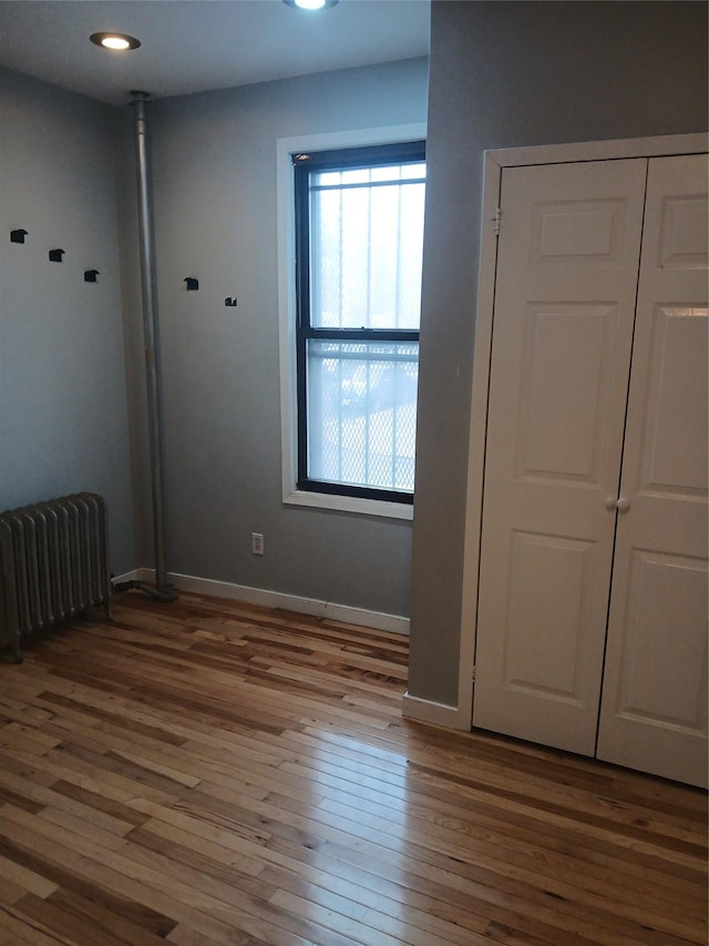 unfurnished bedroom featuring radiator heating unit, baseboards, and wood-type flooring