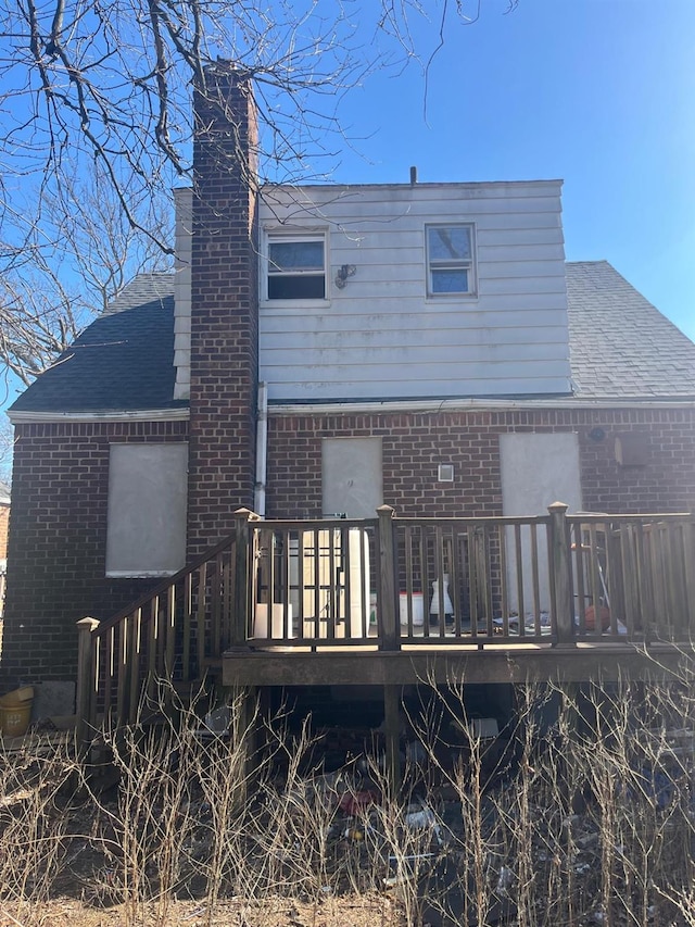 back of house with brick siding, a chimney, a shingled roof, and a wooden deck