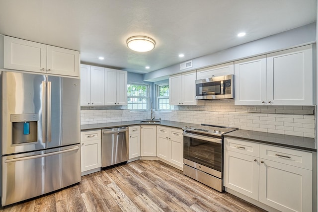 kitchen with visible vents, decorative backsplash, dark countertops, stainless steel appliances, and light wood-type flooring