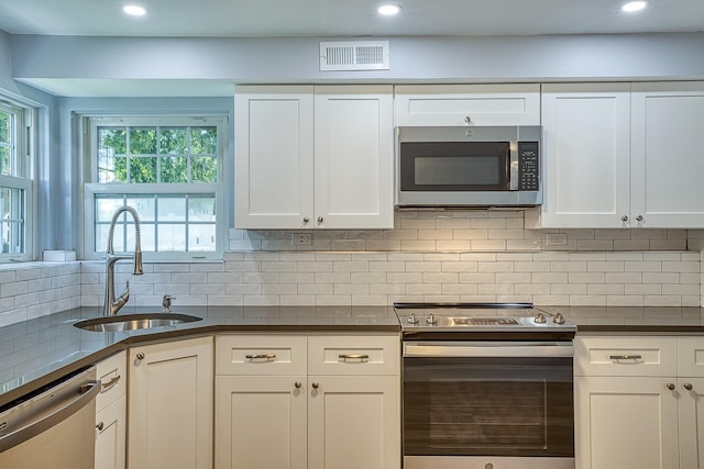 kitchen with dark countertops, visible vents, backsplash, appliances with stainless steel finishes, and a sink