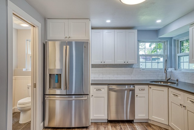 kitchen featuring appliances with stainless steel finishes, dark countertops, a sink, and white cabinetry