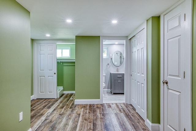 hall with a sink, recessed lighting, wood finished floors, and baseboards