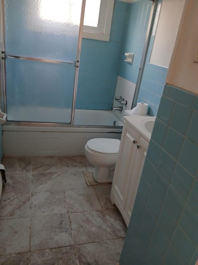 bathroom featuring enclosed tub / shower combo, toilet, tile walls, and vanity