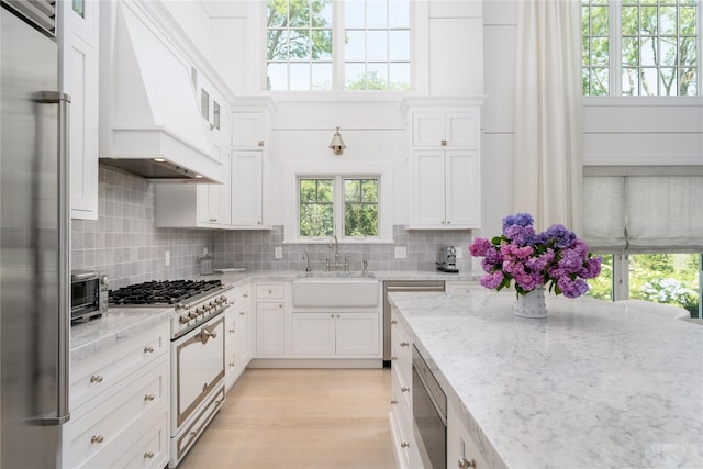 kitchen featuring custom exhaust hood, high end appliances, backsplash, white cabinets, and a sink