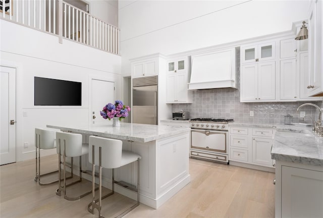 kitchen with a sink, a kitchen island, stainless steel built in refrigerator, range with gas cooktop, and custom range hood