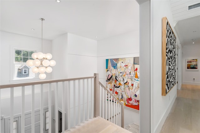 hall featuring a chandelier, baseboards, visible vents, and an upstairs landing