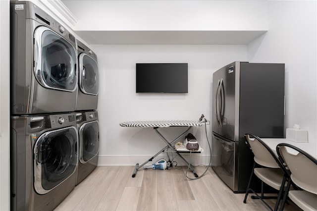 laundry area featuring stacked washer / drying machine, laundry area, light wood-style flooring, and baseboards