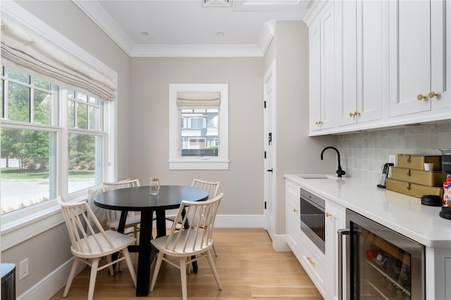 kitchen with beverage cooler, a sink, light wood-type flooring, backsplash, and crown molding