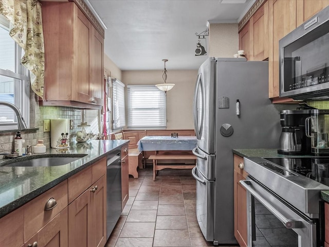 kitchen with light tile patterned flooring, stainless steel appliances, a sink, backsplash, and brown cabinets