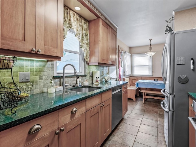 kitchen with dark stone counters, appliances with stainless steel finishes, a sink, backsplash, and light tile patterned flooring