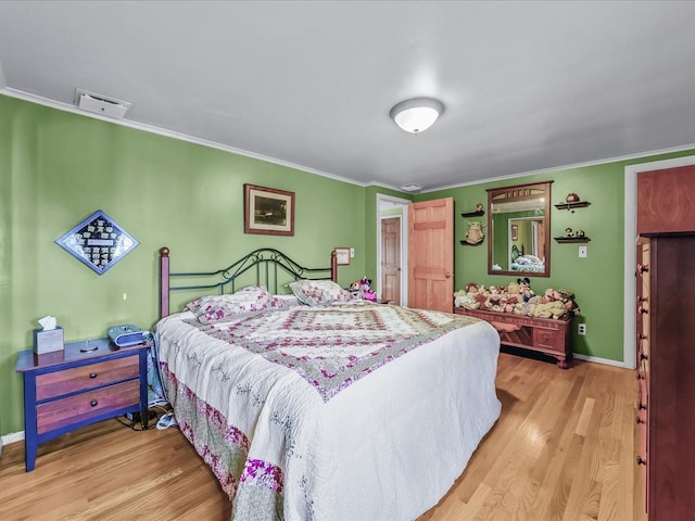 bedroom featuring ornamental molding, light wood-type flooring, visible vents, and baseboards