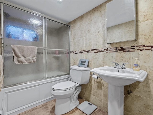 bathroom with toilet, tile patterned flooring, bath / shower combo with glass door, and tile walls