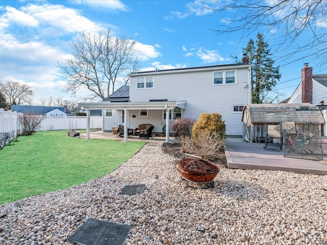 rear view of property featuring a fire pit, solar panels, a fenced backyard, a deck, and a yard