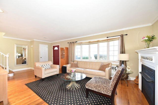 living area with stairway, ornamental molding, wood finished floors, and a glass covered fireplace