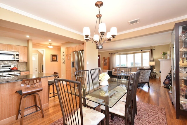 dining space with a chandelier, light wood-type flooring, visible vents, and crown molding