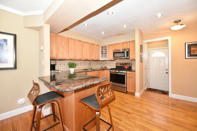 kitchen with stainless steel appliances, backsplash, a sink, a peninsula, and a kitchen bar