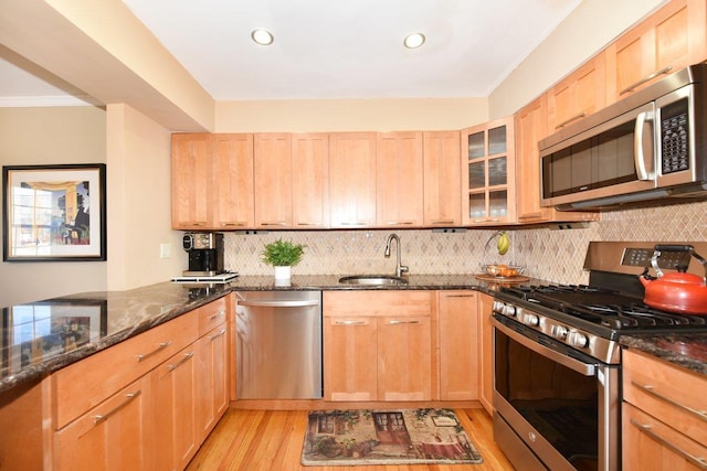 kitchen featuring light wood-style flooring, dark stone countertops, a sink, stainless steel appliances, and backsplash