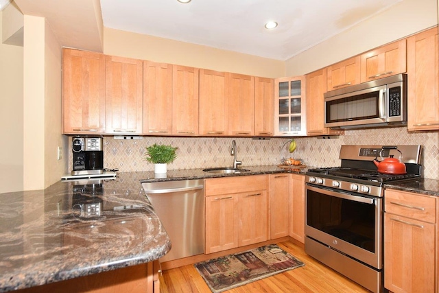 kitchen featuring a sink, appliances with stainless steel finishes, decorative backsplash, light brown cabinetry, and dark stone countertops