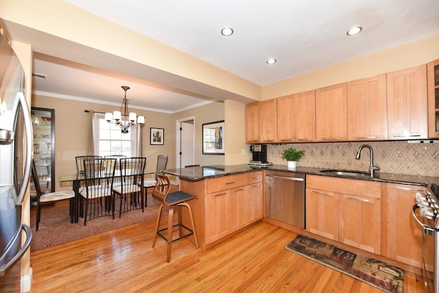 kitchen with light wood finished floors, stainless steel appliances, backsplash, a sink, and a peninsula