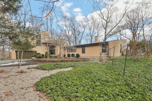 view of front of house featuring stucco siding, driveway, a chimney, and a front yard