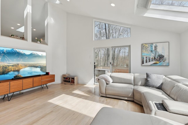 living area featuring a skylight, high vaulted ceiling, wood finished floors, and recessed lighting