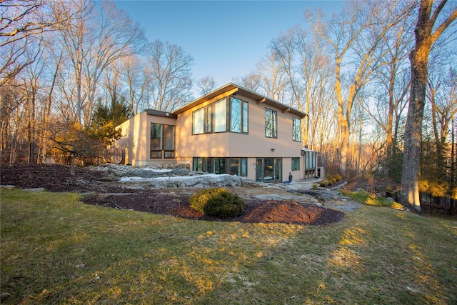 rear view of house featuring a lawn and stucco siding