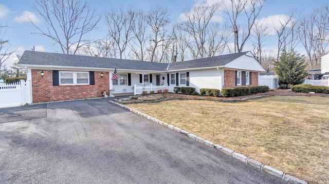 ranch-style home with brick siding, aphalt driveway, fence, a porch, and a front yard