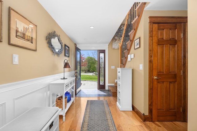 doorway to outside featuring recessed lighting, light wood finished floors, stairs, and a wainscoted wall