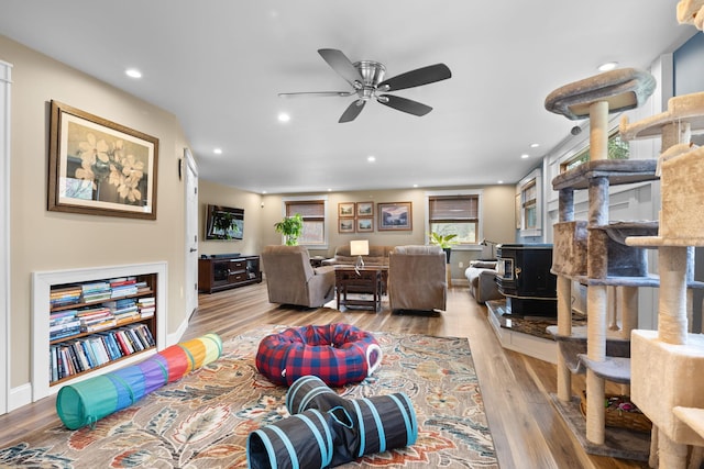 living area featuring ceiling fan, a wood stove, wood finished floors, baseboards, and recessed lighting