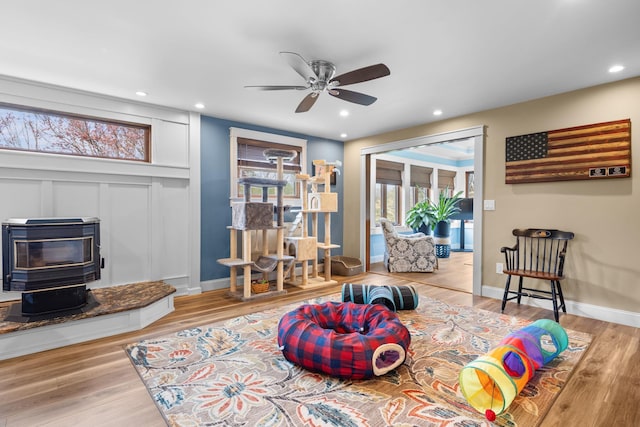 sitting room with a ceiling fan, a wood stove, recessed lighting, and wood finished floors