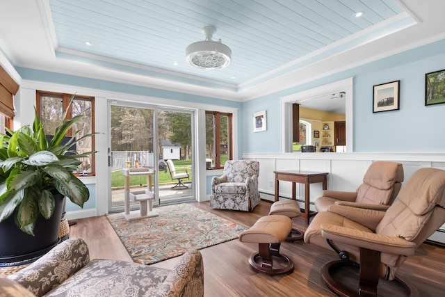 living room with a wainscoted wall, ornamental molding, a tray ceiling, and wood finished floors
